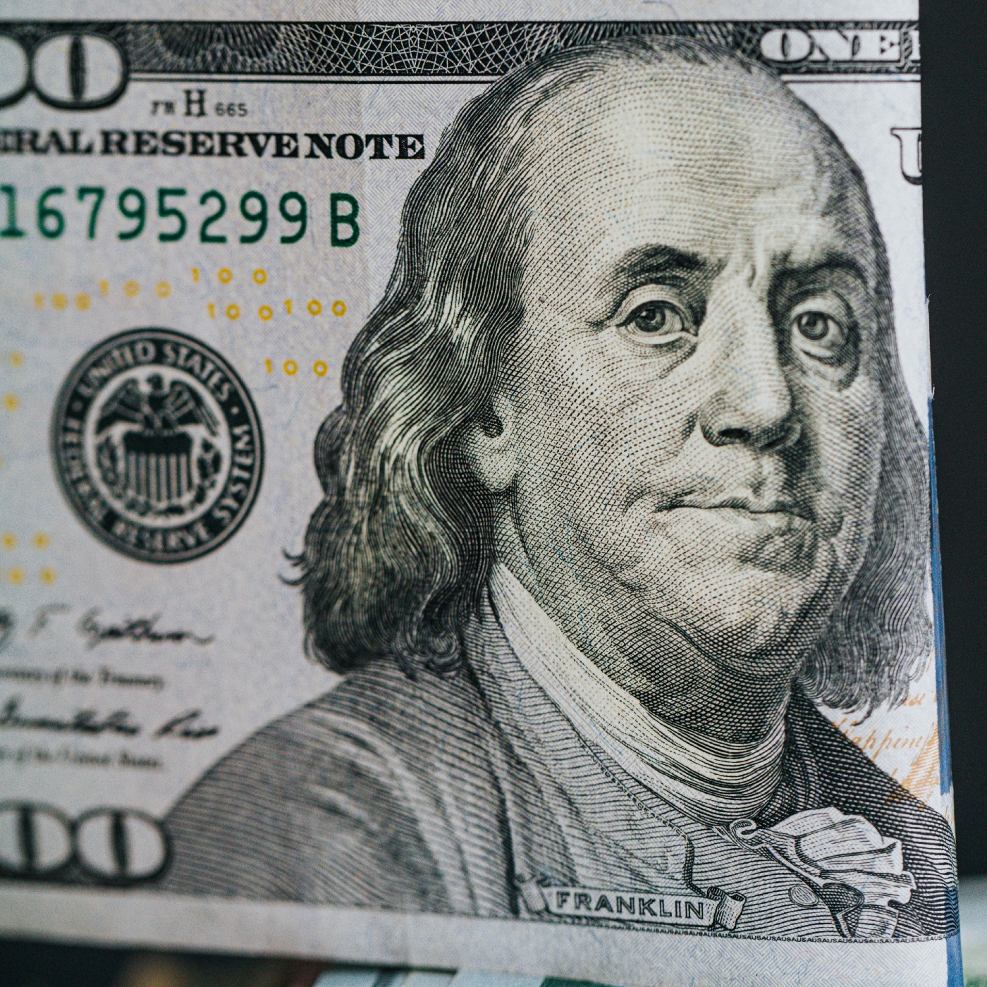 Enlarged photo of a one hundred dollar bill prominently featuring the face of Ben Franklin.