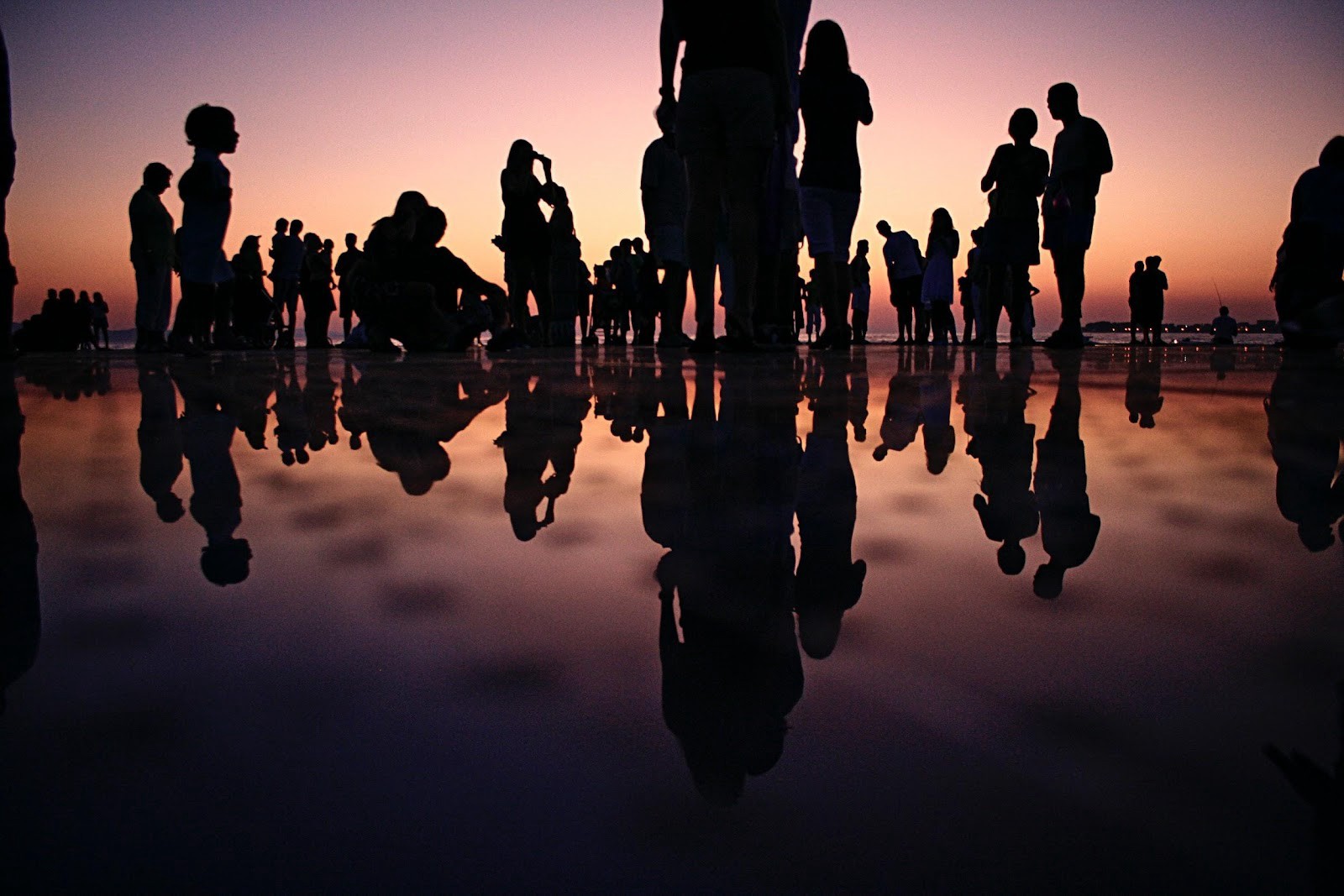 Crowd gathered on beach at sunset.
